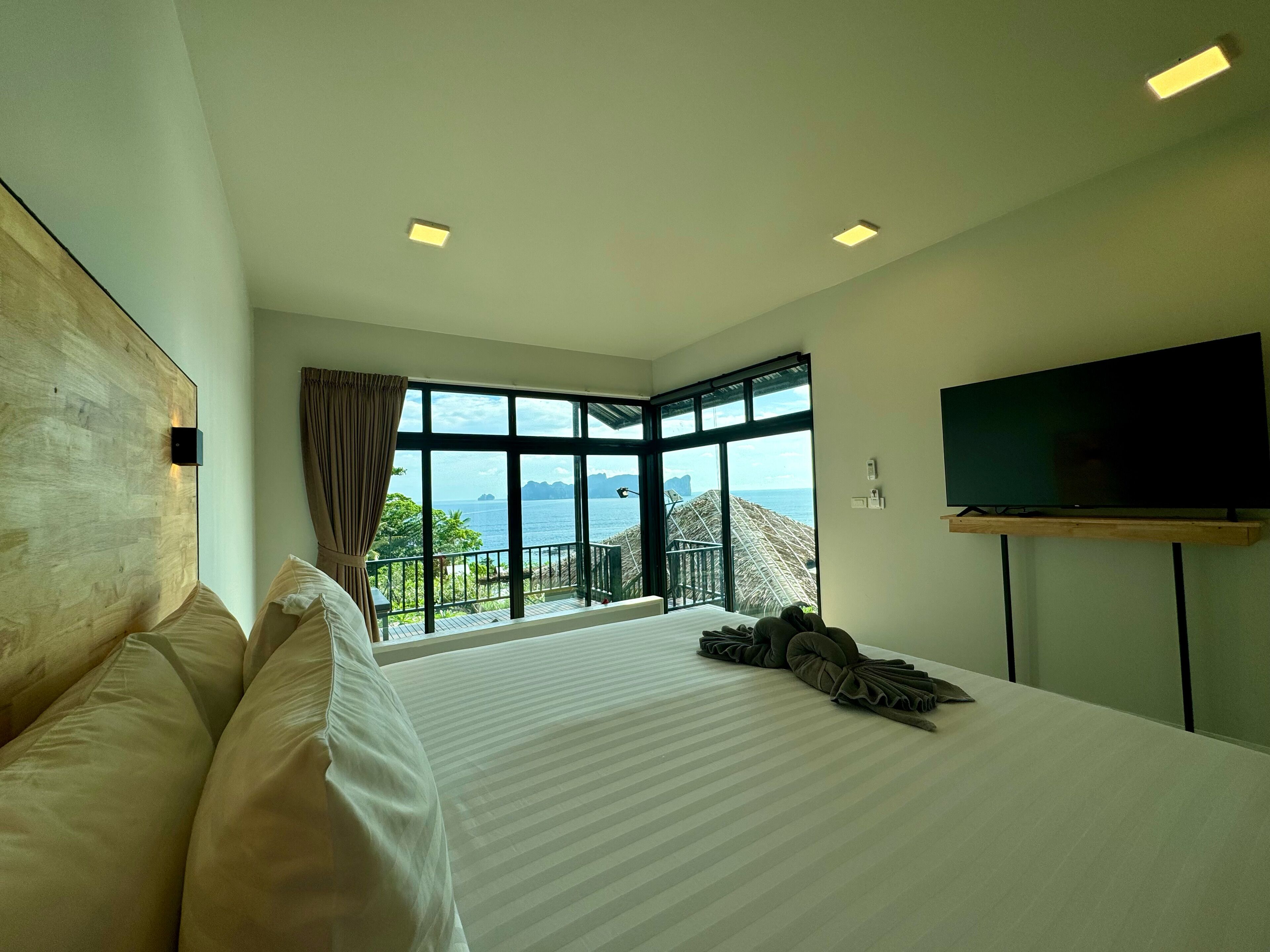 Un hotel moderno con una cama grande, un televisor montado en la pared y vistas al mar a través de amplias ventanas.