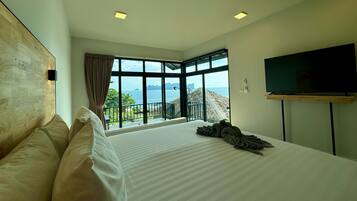 Un hotel moderno con una cama grande, un televisor montado en la pared y vistas al mar a través de amplias ventanas.