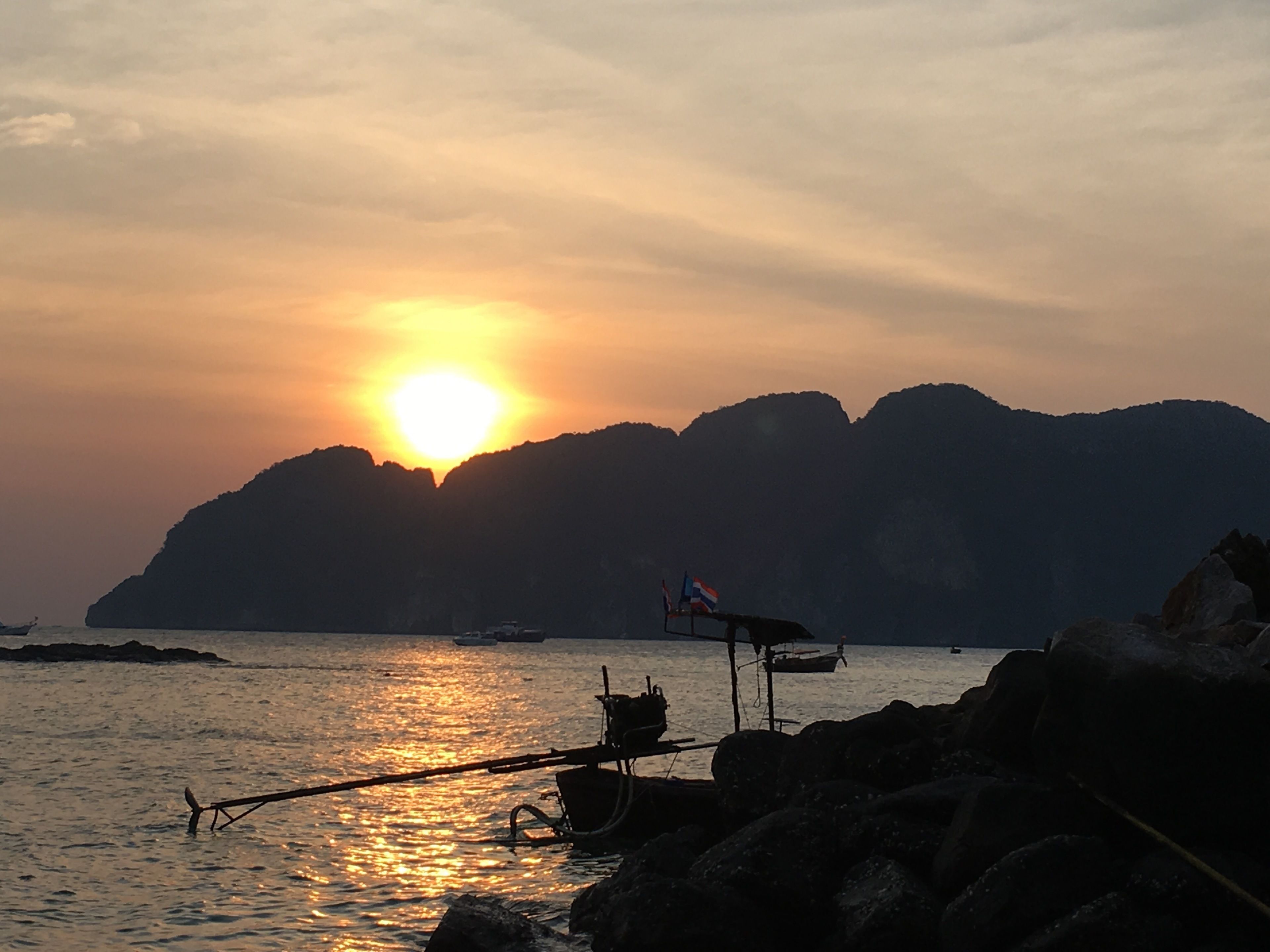 Ein Sonnenuntergang über einem ruhigen Meer mit Booten und felsiger Küste.
