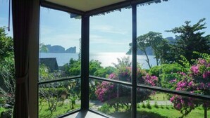 A room with large windows offering a view of a lush garden and a body of water.
