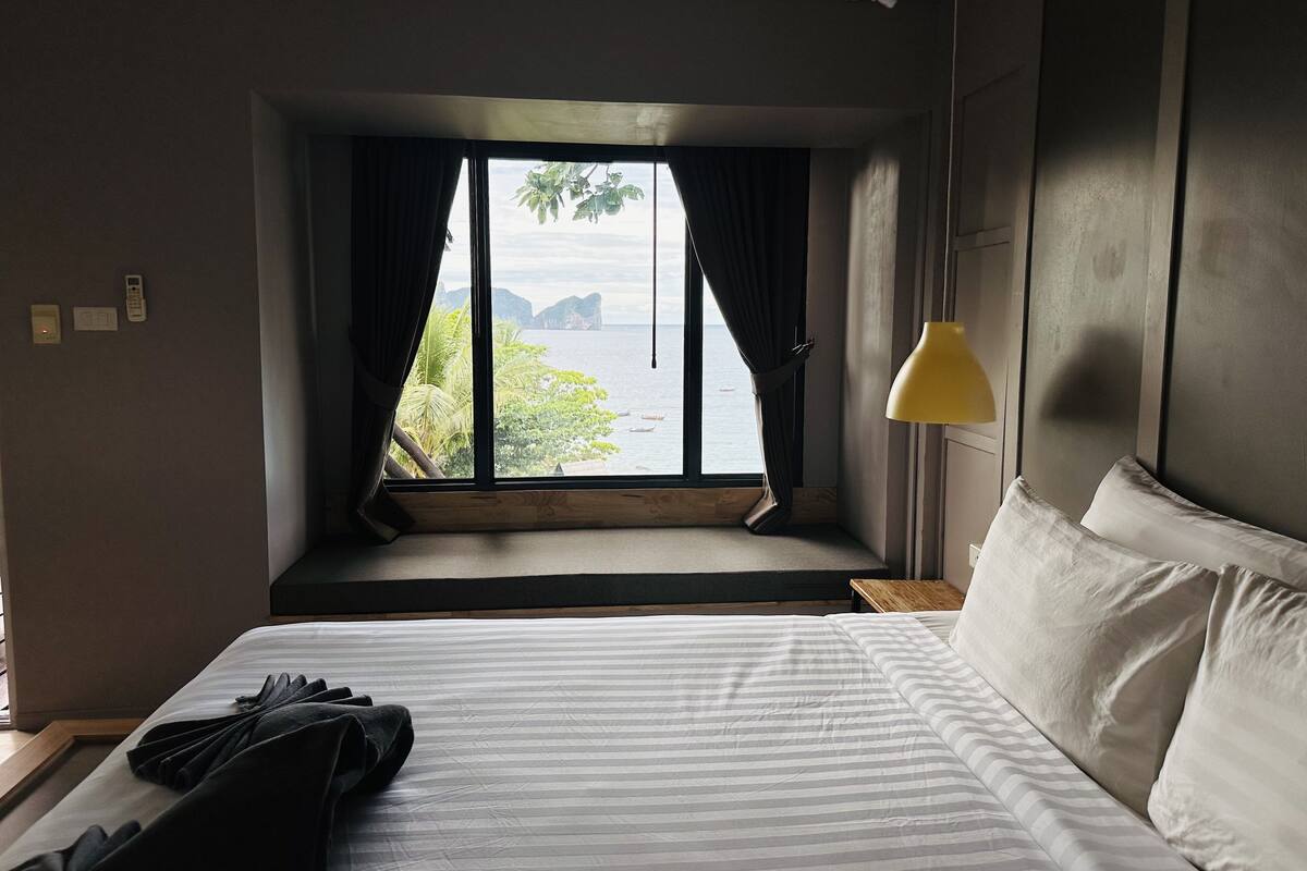 Een hotelkamer met een groot bed, een raam met gordijnen, een nachtkastje en een lamp.