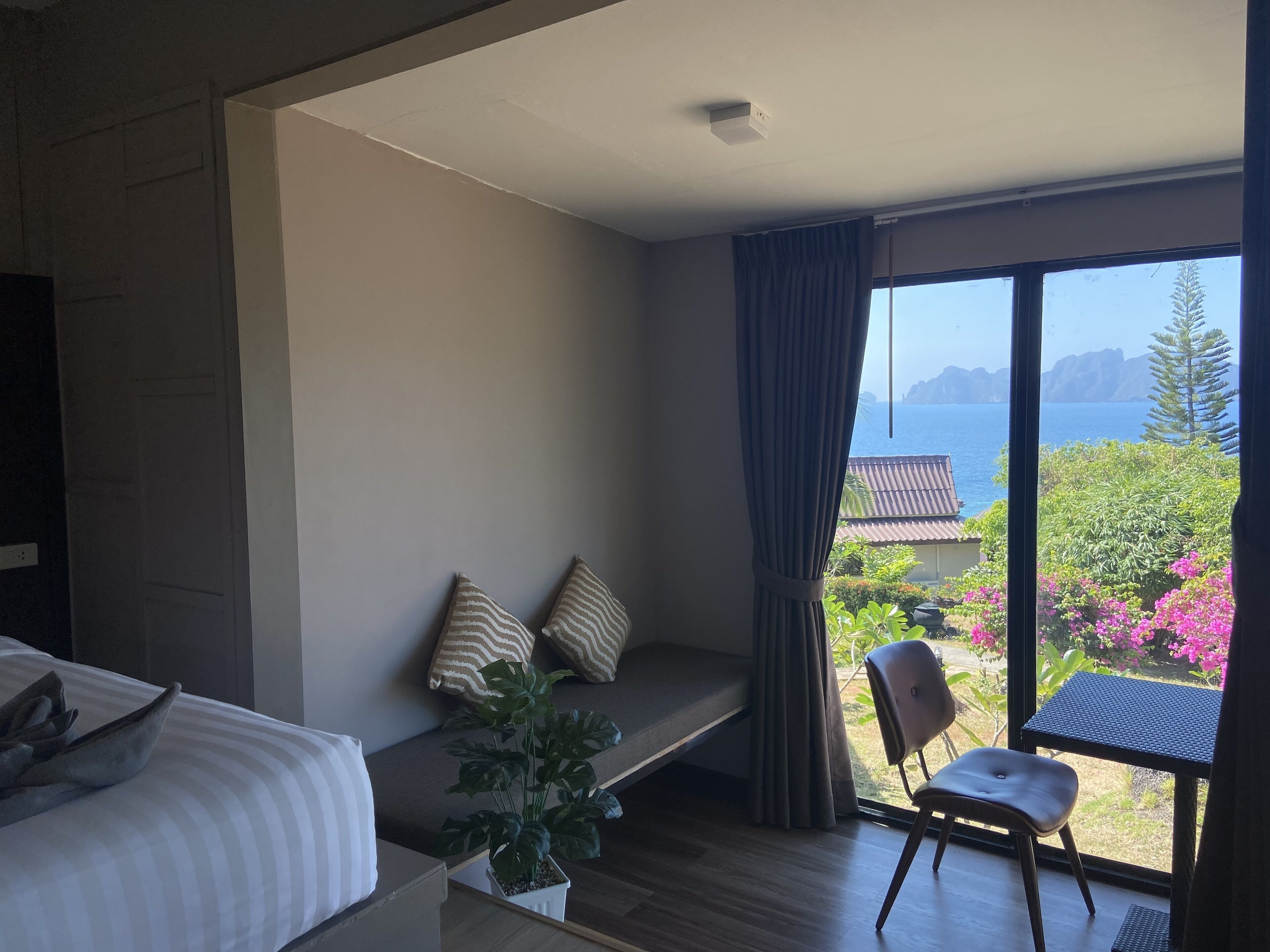 A room with a bed, a window with curtains, a small table, and a chair.