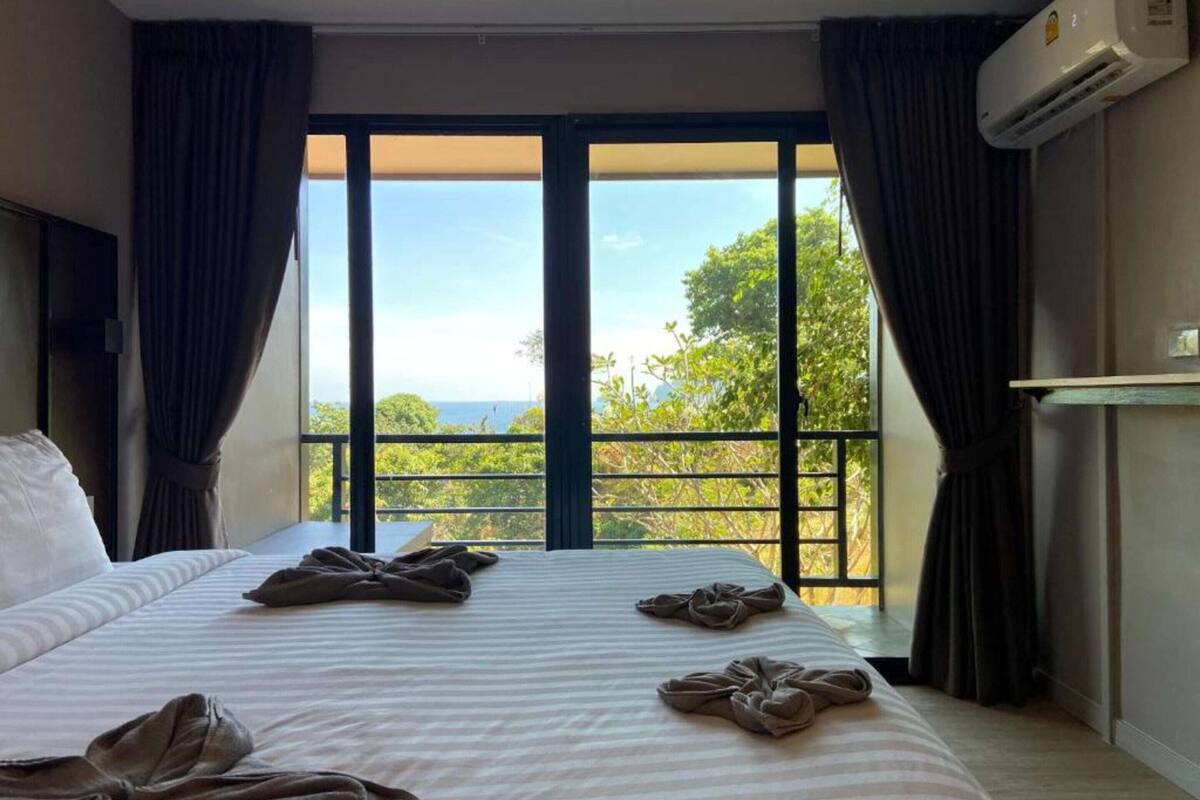 Een hotelkamer met een groot bed, een flatscreen televisie, een airconditioning en een balkon met uitzicht op zee.