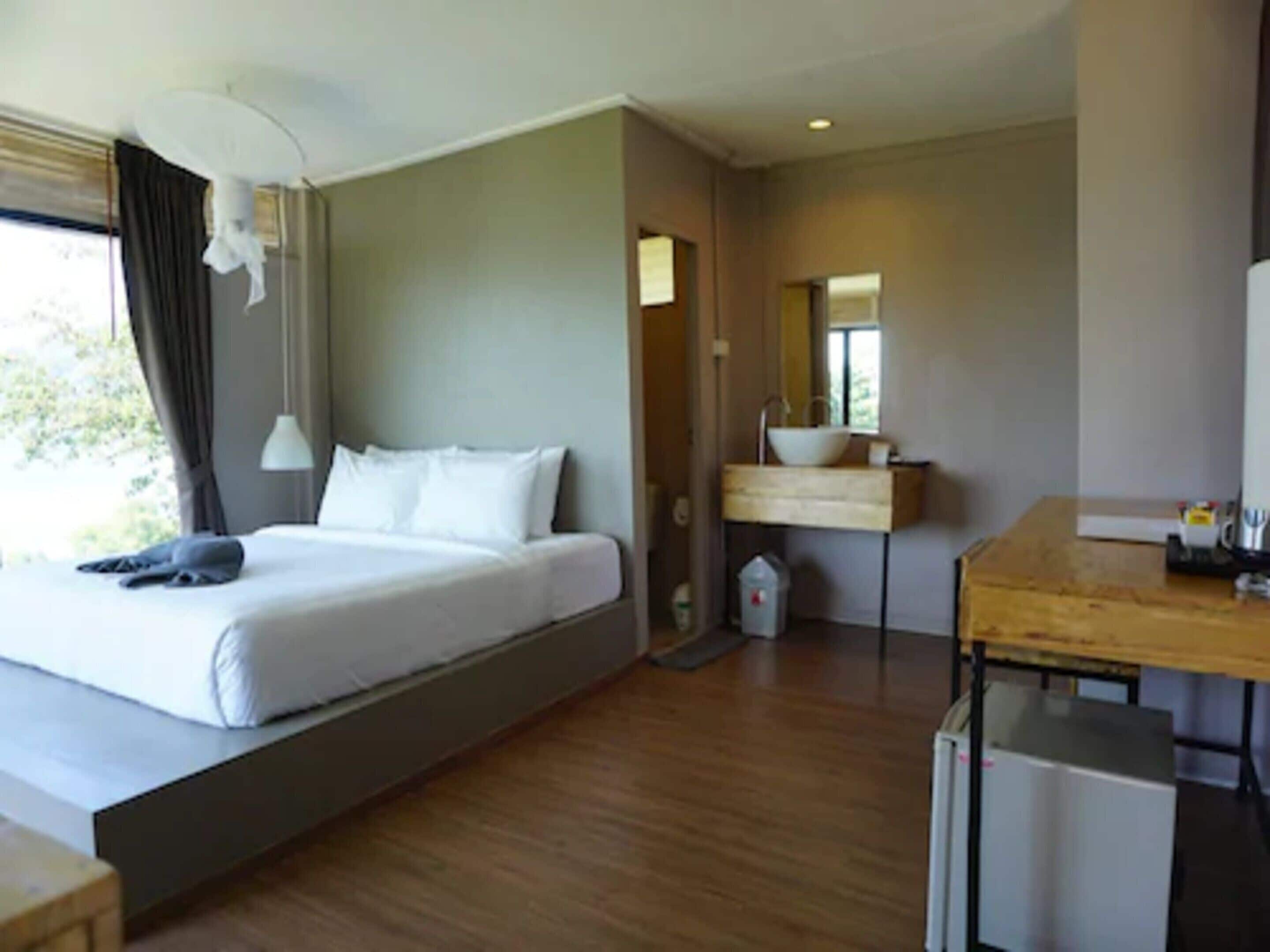 Una habitación de hotel moderna con una cama grande, un escritorio de madera, un lavamanos y un espejo.