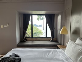 A hotel room with a bed, a window with curtains, a bedside lamp, and a view of the sea and mountains.