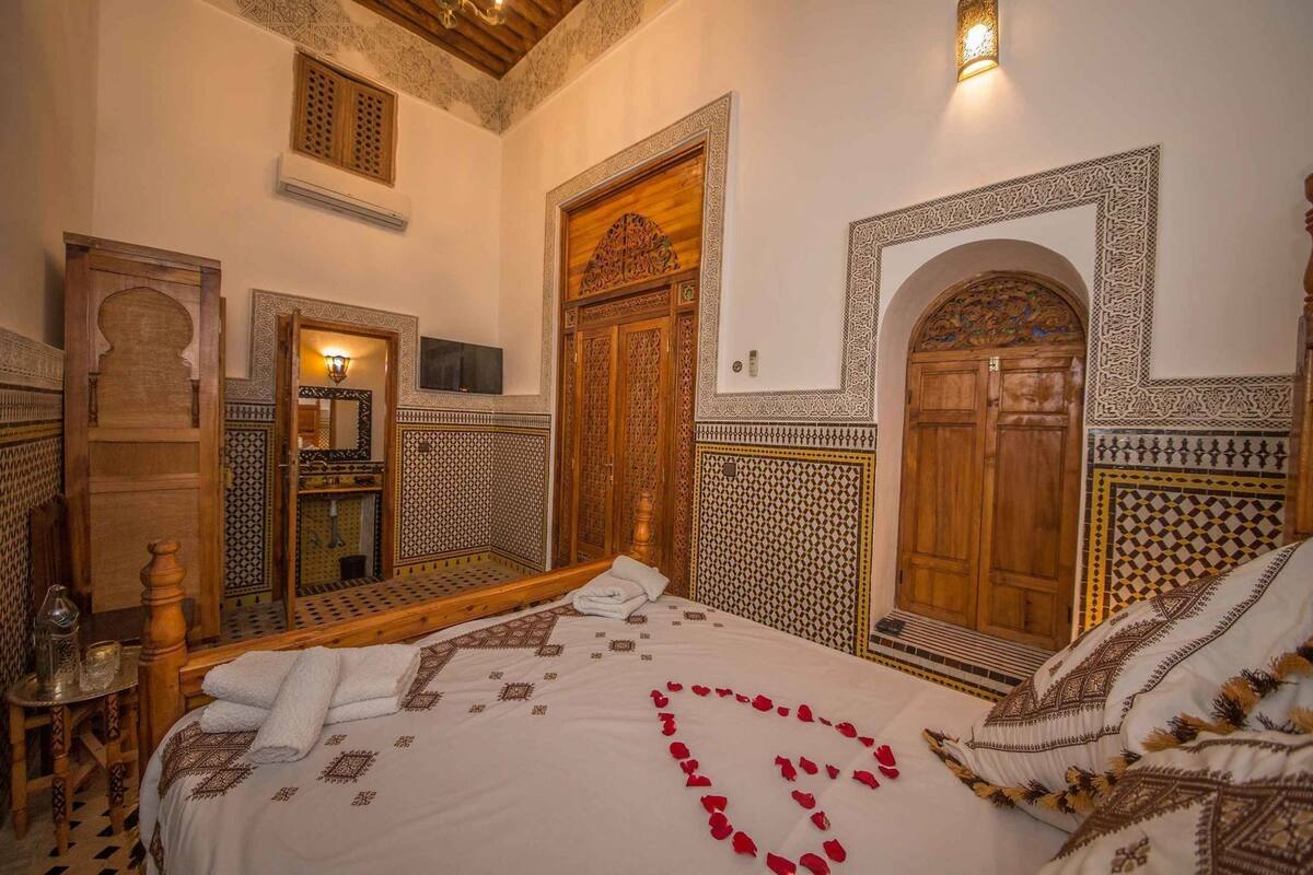 A traditional Moroccan room with a bed, wooden doors, and intricate tile work.