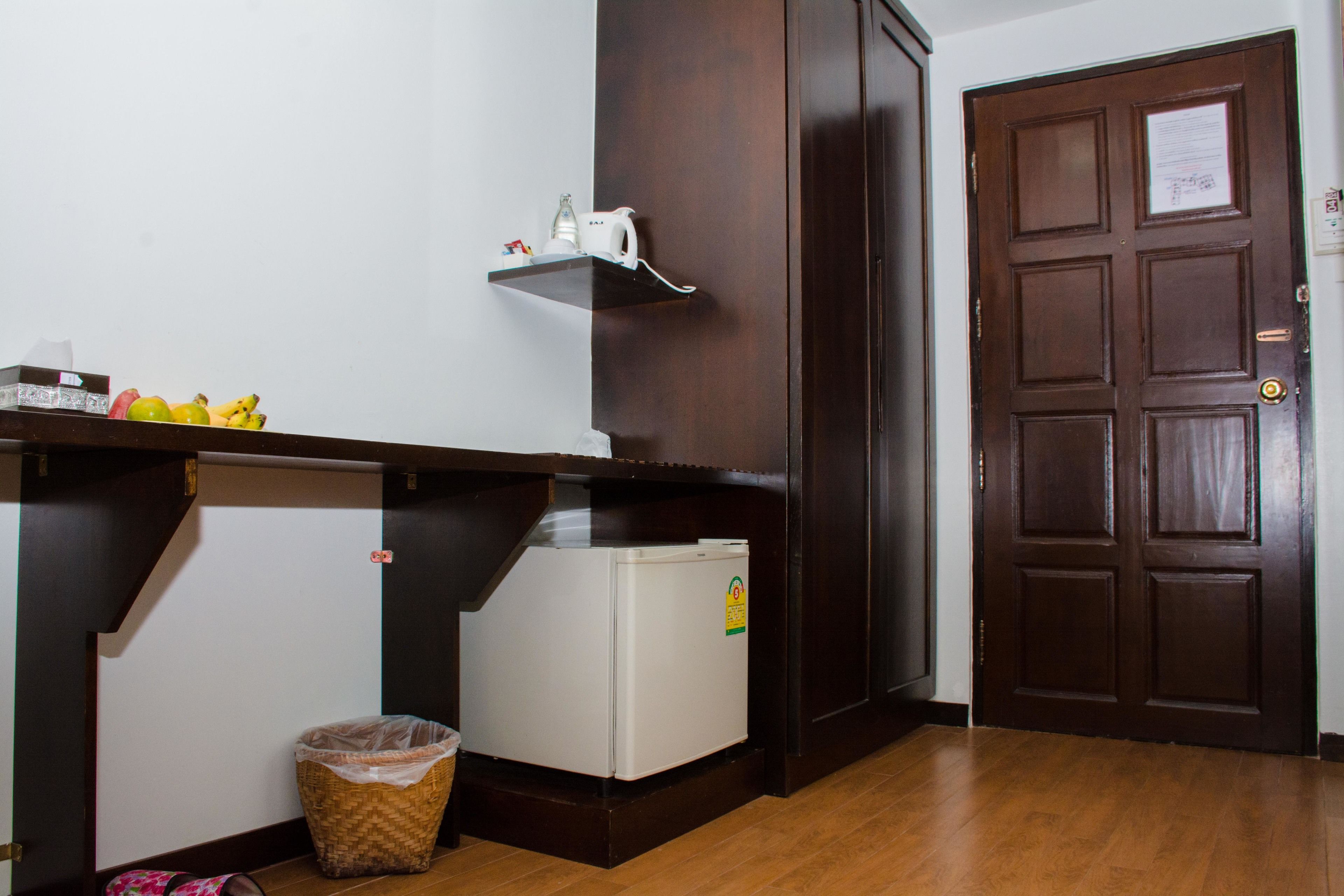 A compact kitchen with a refrigerator, a wooden cabinet, and a small trash bin.