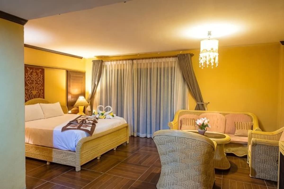 Una habitación de hotel con cama, una silla, una mesita y una araña.