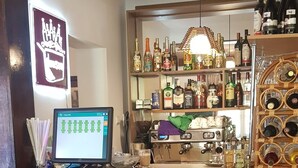 Un espace bar équipé d’un écran d’ordinateur, d’étagères remplies de bouteilles d’alcool et d’une variét é de collations et de desserts disposés sur une table de buffet.