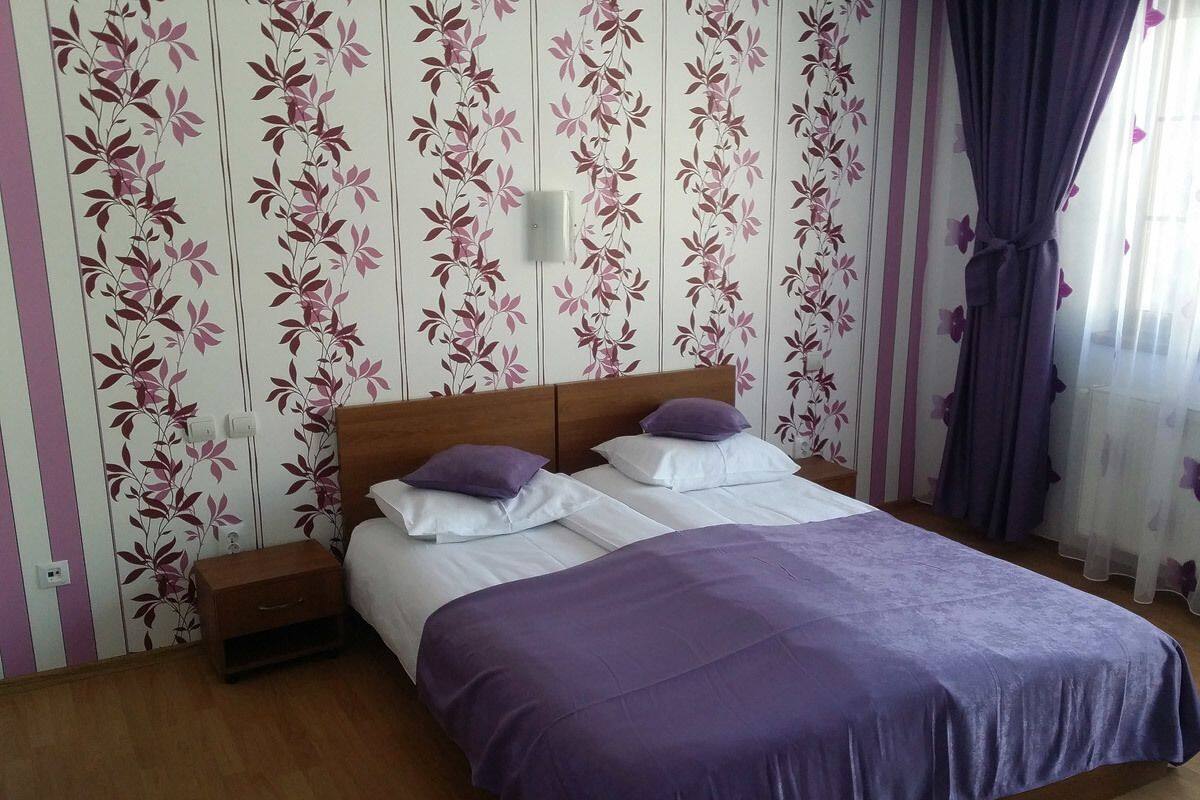 A bedroom with a bed, two bedside tables, a nightstand, and a window with curtains.