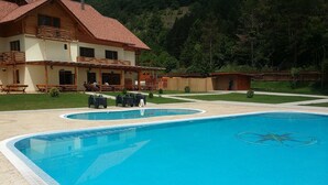 Une piscine dotée d’une terrasse en bois et de chaises longues, entourée d’une maison dont le toit est recouvert de tuiles rouges.