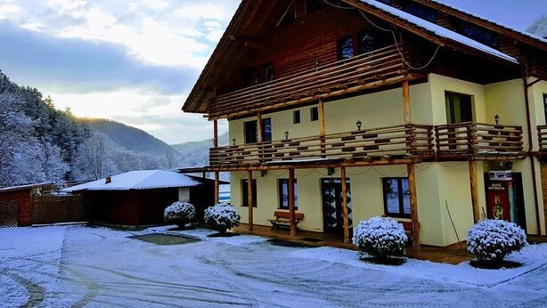 Un bâtiment en bois à deux étages, doté d’un balcon, entouré d’arbres couverts de neige et avec une montagne en arrière-plan.