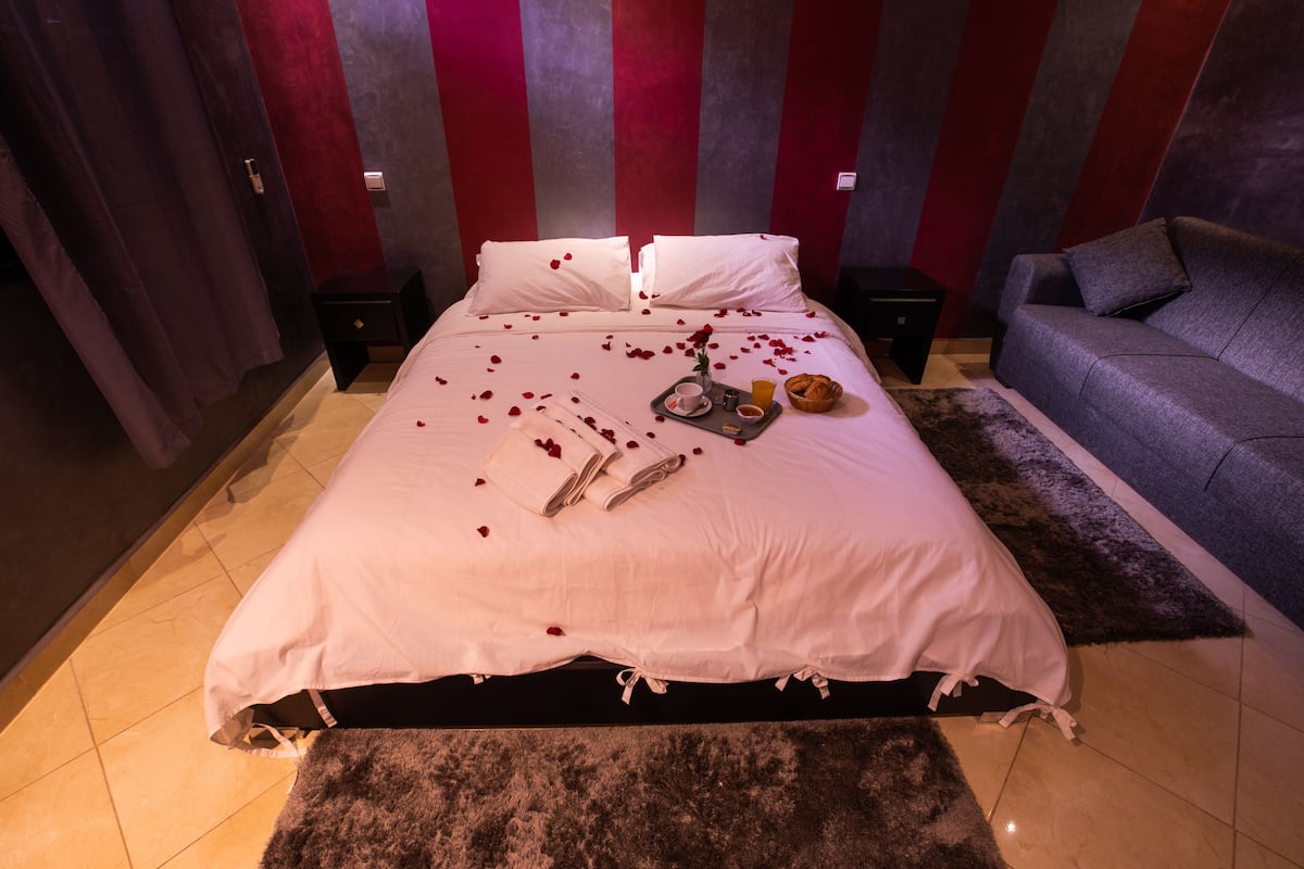 A neatly made bed with white linens, a tray with breakfast items, and rose petals scattered on the bed.