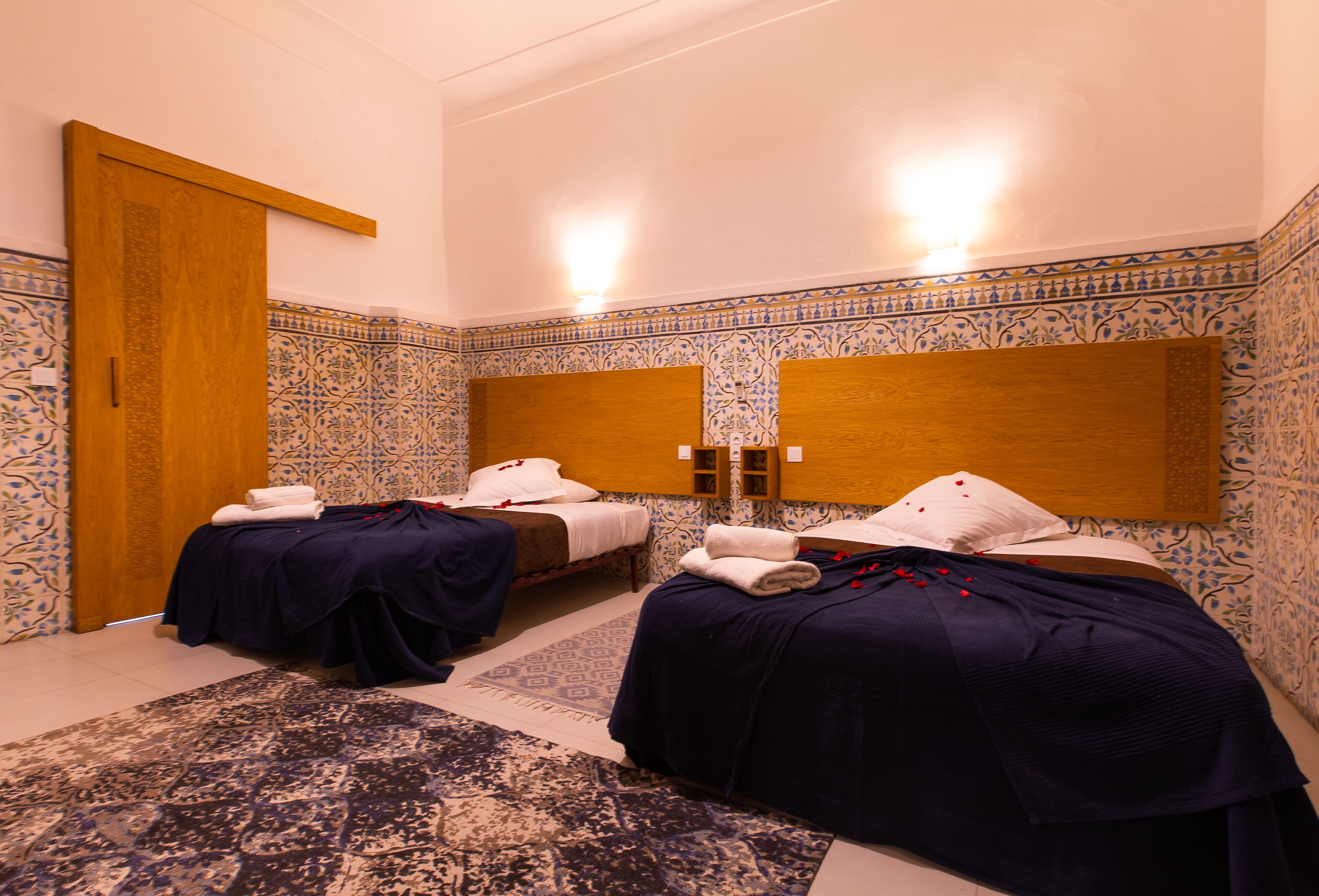 A room with two beds, a wooden headboard, patterned walls, and a door.