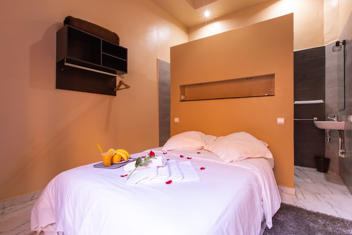 A hotel room with a bed, a small shelf, a bathroom with a sink, and a mirror.