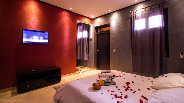 A modern bedroom with a bed, a TV, a console, and a bathroom visible through an open door. - Hotel Toulousain (Marrakech)