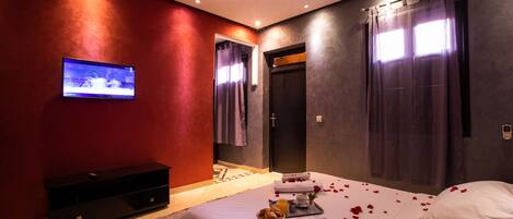 A modern bedroom with a bed, a TV, a console, and a bathroom visible through an open door.