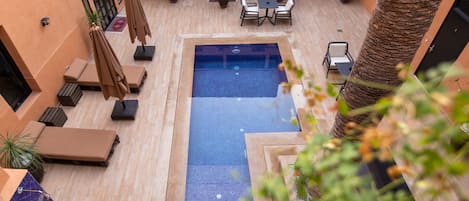 Un área de piscina en la azotea con sillones, una mesa y plantas en macetas.