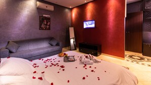Una habitación de hotel con una cama, un sofá gris, un televisor y una pared roja.