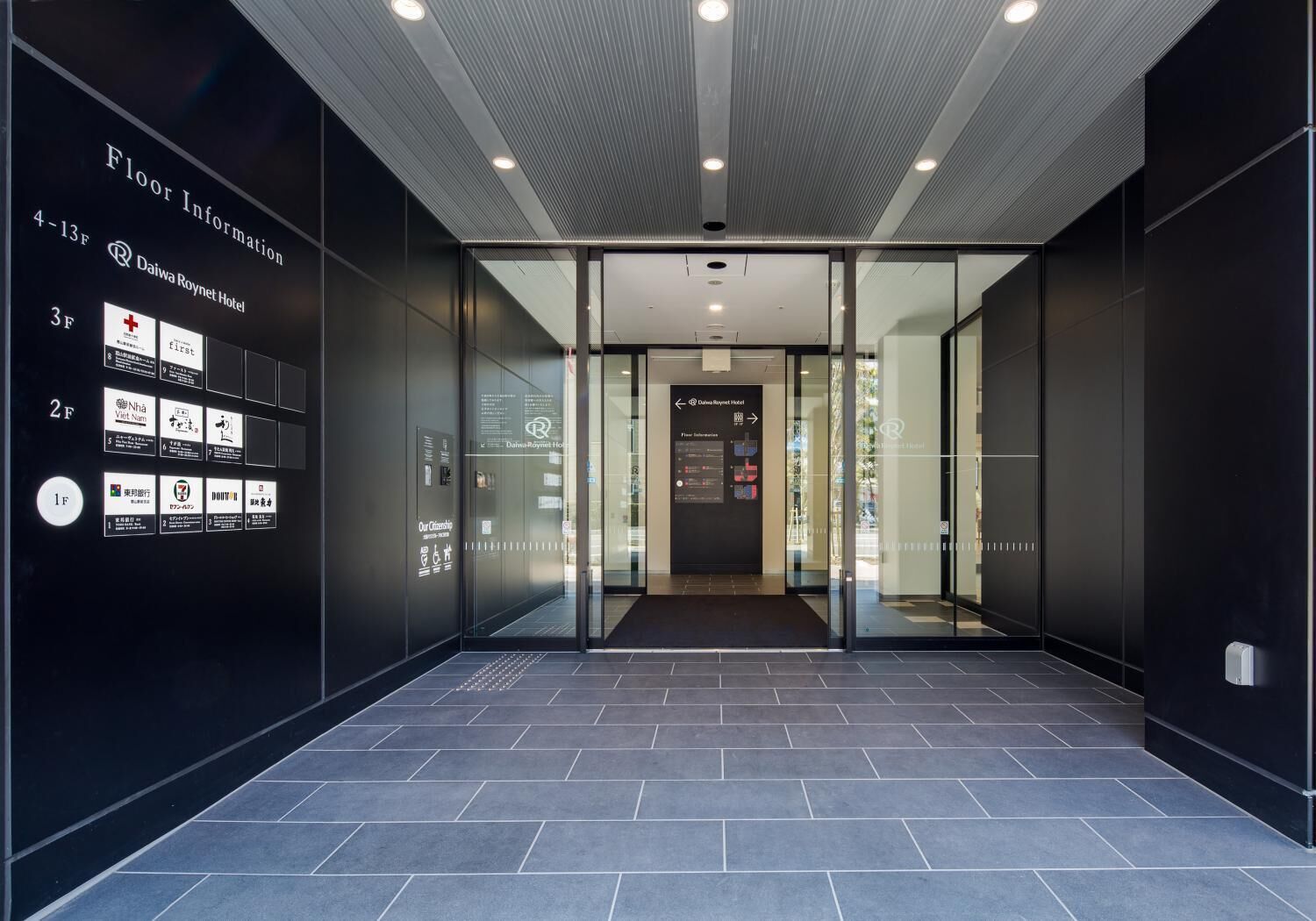 Un hall d’hôtel moderne avec un plan d’étage clair affiché au mur, un comptoir d’accueil et une entrée en verre.
