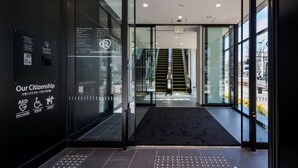 Entrada de un hotel moderno con puertas de cristal, una rampa y un cartel con información de emergencia.