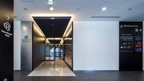 Un moderno vestíbulo de hotel con un puerta de cristal que da al área de recepción, un diseño mural en blanco y negro, y un cartel con el plano del hotel a la derecha.
