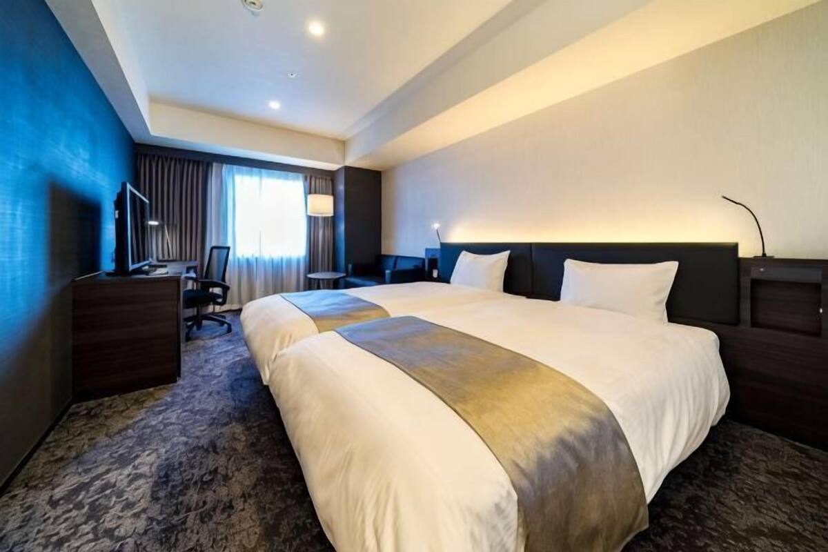 Habitación de hotel con una cama grande, un escritorio, una silla, un aparador y una ventana con cortinas.