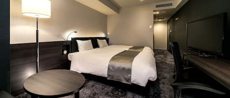 Habitación de hotel con cama, escritorio, silla, televisor y lámpara.