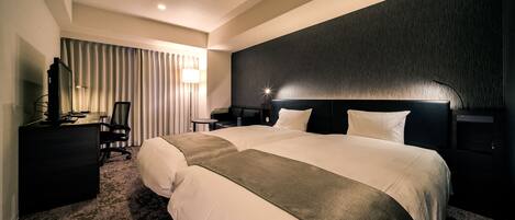 A modern hotel room with a large bed, a desk with a computer, and a chair.