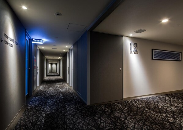 Un pasillo de hotel con alfombra estampada, paredes azules y puertas numeradas.