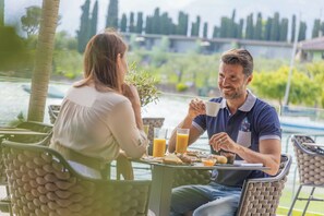 Een stel aan het dineren aan een buitentafel, met uitzicht op water en groen.