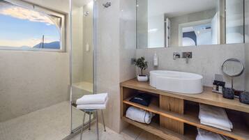 A modern bathroom with a glass shower enclosure, a large mirror, a white sink, and a wooden vanity with shelves.