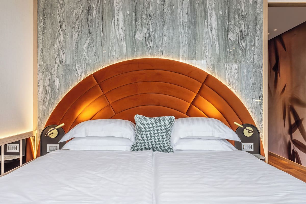 Een bed met een marmeren hoofdbord, witte beddengoed en twee nachtkastjes met klokken.