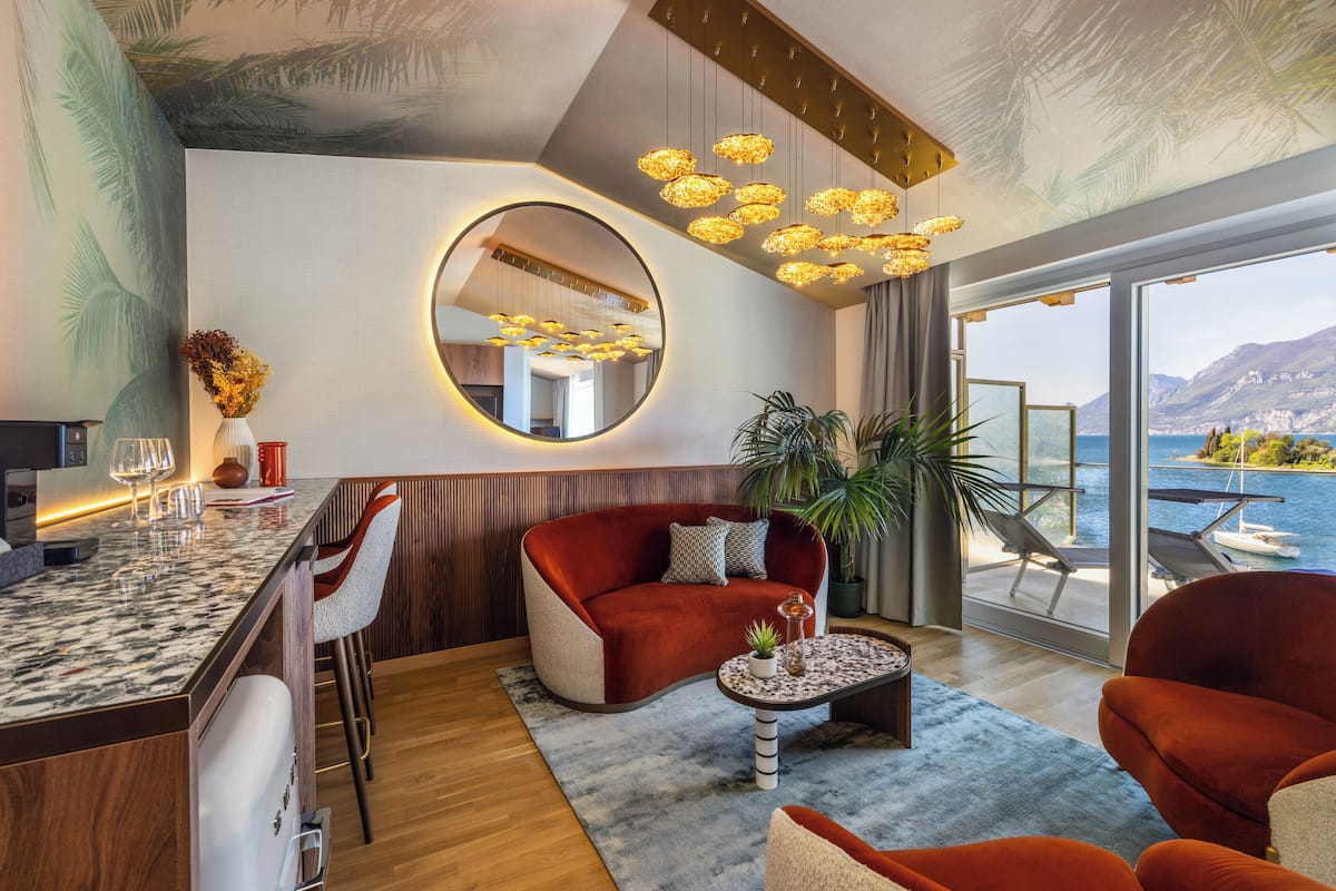 Een moderne woonkamer met een rode bank, een ronde spiegel en uitzicht op zee door grote ramen.