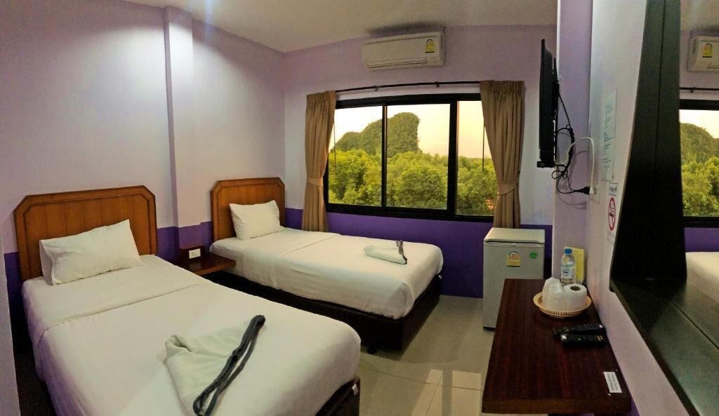 Quarto de hotel com duas camas de solteiro, uma pequena escrivaninha com cadeira, televisão e janela com vista para árvores.