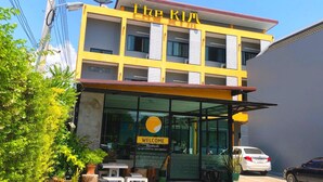 Un hotel llamado "The K1" con fachada amarilla, entrada de vidrio y un cartel dando la bienvenida a los huéspedes.