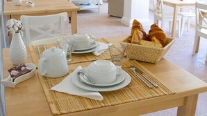 Een ontbijttafel gedekt met witte borden, bekers en een mandje croissants.