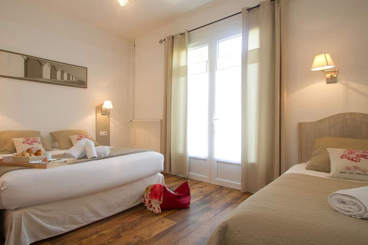Quarto de hotel com duas camas, uma janela grande com cortinas, luminárias fixadas na parede e uma moldura com imagem.
