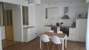 Een kleine keuken met witte kasten, een houten eettafel en vier witte stoelen.