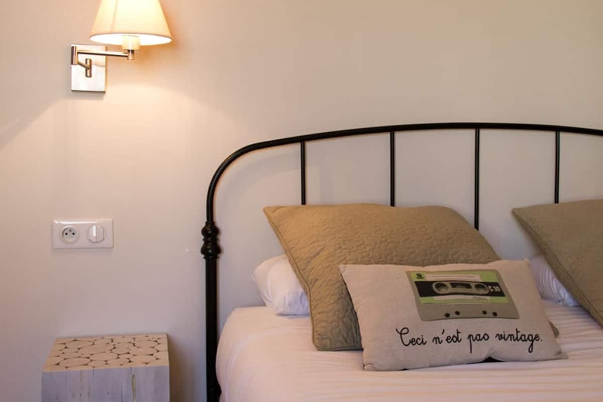 Uma cama bem arrumada com cabeceira, luminária de cabeceira e tomada na parede.