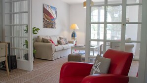 Een woonkamer met een bank, een rode fauteuil, een lamp en een schilderij aan de muur.