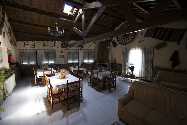 Un comedor amplio con mesas y sillas de madera, un techo alto con vigas a la vista y un gran ventanal que proporciona luz natural.