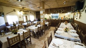 Un restaurante con varias mesas dispuestas, cubiertas con manteles blancos, sillas de madera y diversos elementos de mesa, incluyendo platos, vasos y cubiertos.
