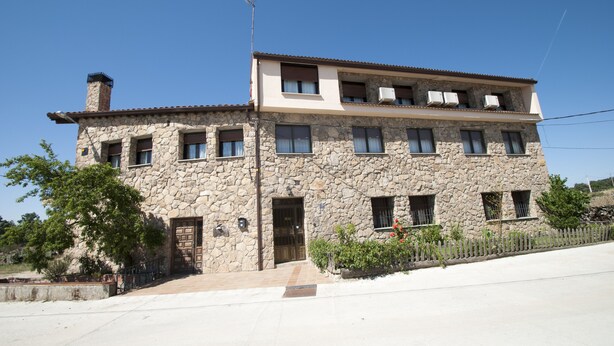 Un edificio de piedra de dos pisos con techo plano, varias ventanas y un pequeño porche.