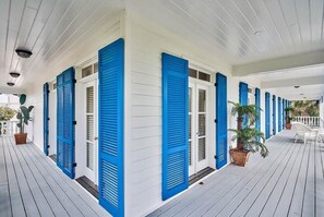 Eine überdachte Veranda mit weißen Wänden und blauen Fensterläden, mit Topfpflanzen und einem weißen Stuhl.