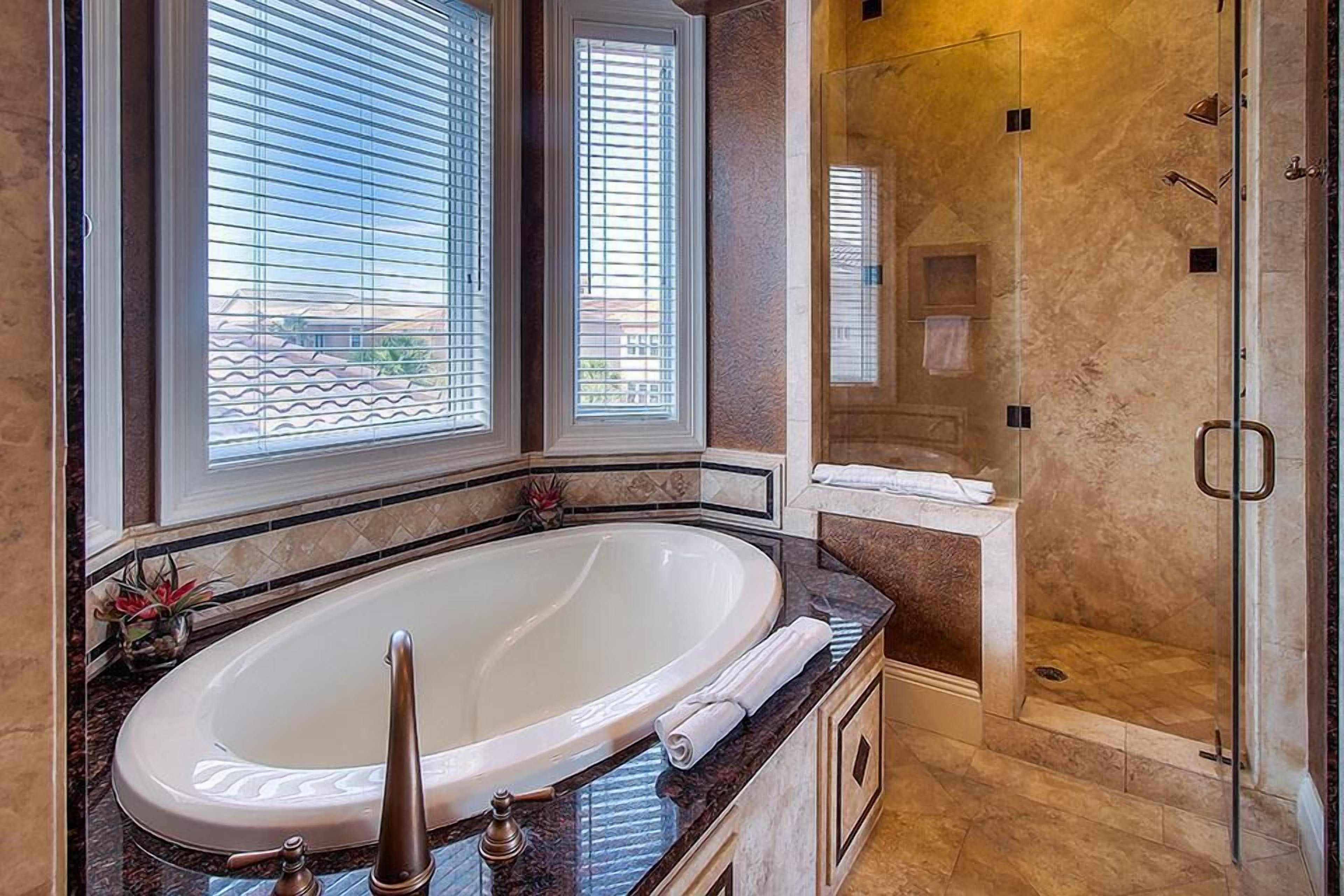 A bathroom with a large bathtub, a glass shower enclosure, and a window with blinds.