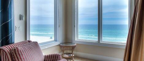 A room with a striped sofa and a small table, large windows with a view of the ocean.
