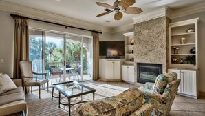 A living room with a glass coffee table, a sofa, a patterned armchair, a television, a fireplace, and a balcony with curtains. - Casa de Fiesta 5 Bedroom Holiday Home by Five Star Properties (Destin)