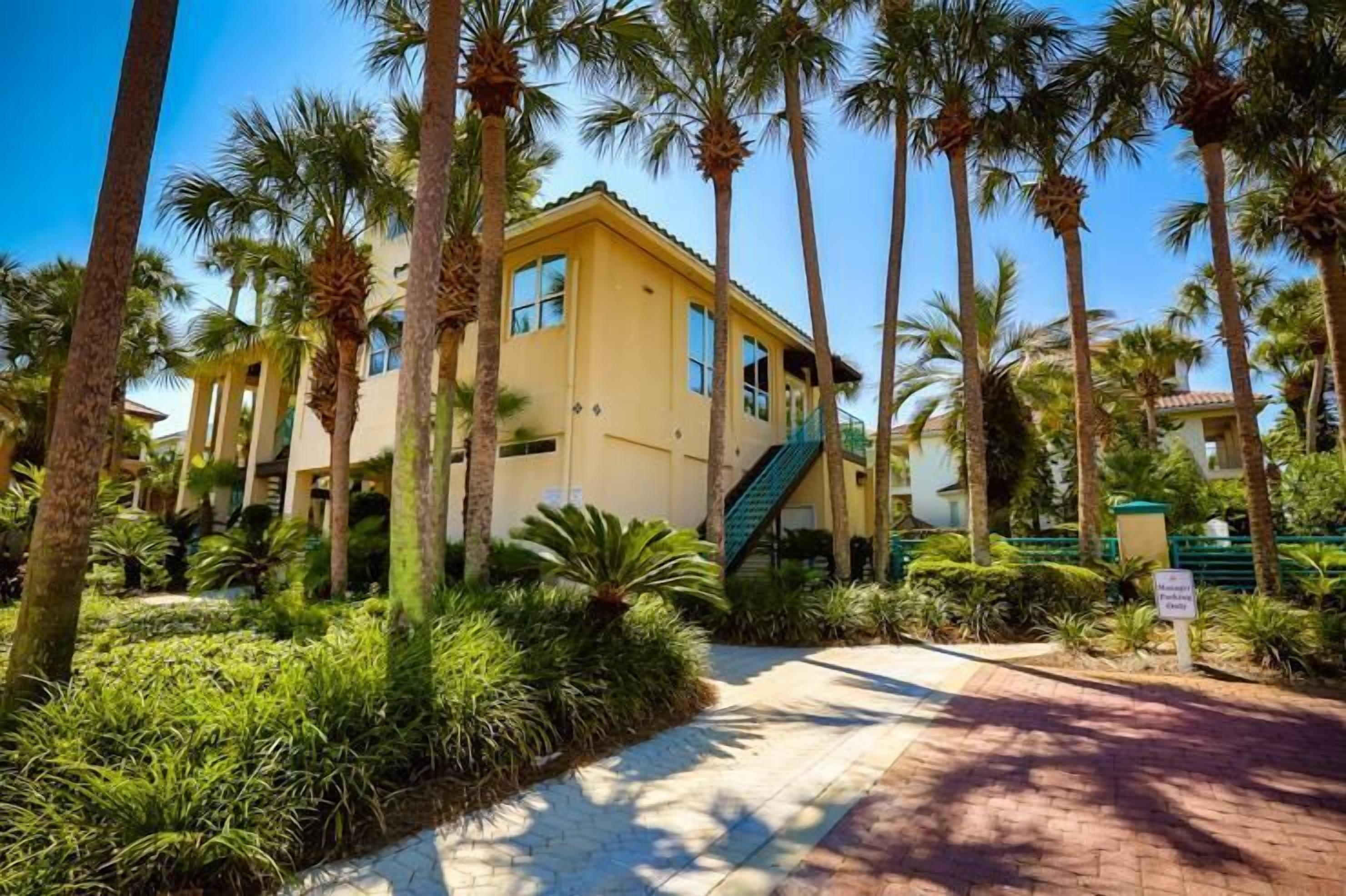 A yellow building with a staircase, surrounded by palm trees and greenery.