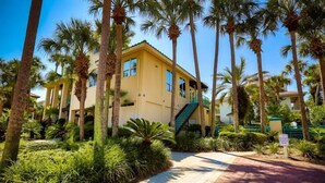 A yellow building with a staircase, surrounded by palm trees and greenery. - Casa di Tramonto 6 Bedroom Holiday Home by Five Star Properties (Destin)